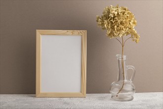 White wooden frame mockup with dried hydrangea in glass on beige paper background. Blank, vertical