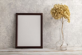 Brown wooden frame mockup with dried hydrangea in glass on gray concrete background. Blank,