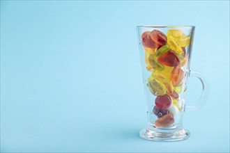 Various fruit jelly candies in drinking glass on blue pastel background. side view, copy space