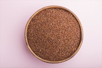 Wooden bowl with raw red quinoa seeds on a pastel pink background. Top view, flat lay, close up