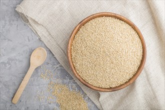 Wooden bowl with raw white quinoa seeds and wooden spoon on a gray concrete background and linen