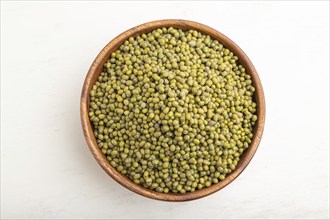 Wooden bowl with raw green mung bean on a white wooden background. Top view, flat lay, close up