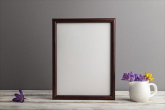 Brown wooden frame mockup with snowdrop crocus flowers on gray paper background. Blank, vertical