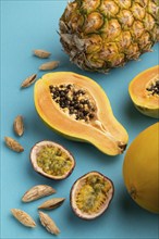 Ripe cut papaya, pineapple, melon, passion fruit, almonds on blue pastel background. Side view,