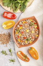 Buckwheat porridge with vegetables in clay bowl on a gray concrete background and linen textile.