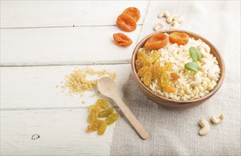 Bulgur porridge with dried apricots, raisins and cashew in wooden bowl on a white wooden background