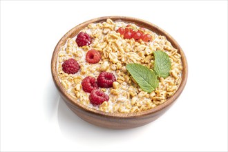 Wheat flakes porridge with milk, raspberry and currant in wooden bowl isolated on white background.