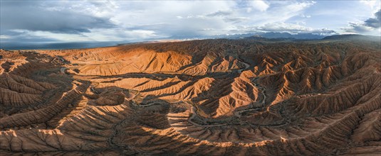 Panorama, landscape of eroded hills at Lake Issyk Kul, badlands at sunset, mountain peaks of the