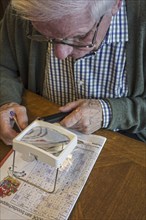 Elderly man suffering from presbyopia, myopia, short-sightedness looking at crossword puzzle though