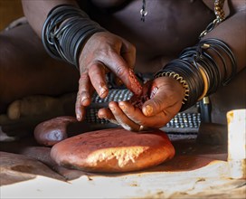 Hands of a Himba woman with ochre paint, Traditional Himba woman makes ochre paint from fat and