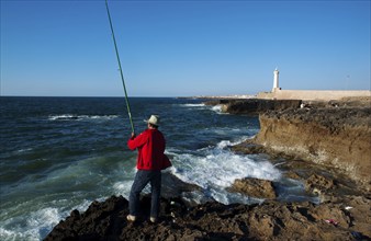 Man fishing in the Atlantic ocean (Rabat, Morocco), In the background, the Rabat lighthouse