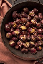 Roasted chestnuts, in an iron pan, wooden table, top view, no people, rustic style