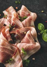 Raw bacon, sliced, with micro greenery and spices, on a black background, close-up