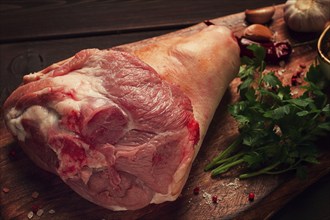 Raw pork knuckle, on a wooden chopping board, with spices, close-up, top view, no people