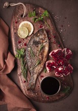 Fried dorado fish, with spices and herbs, on a wooden board, pomegranate sauce, close-up, no people