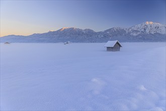 Hut in the snow in front of mountains, evening light, view of Rabenkopf and Jochberg, Schlehdorf,