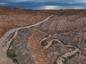 River bed runs through a landscape of eroded hills, badlands, Issyk Kul Lake in the background,