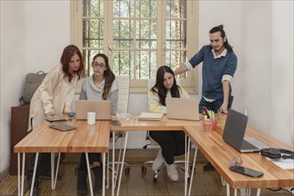 A group of four colleagues collaborating in an office, focused on their laptops. The well-lit room