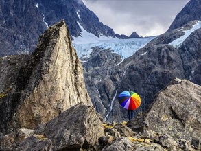 Woman with colorful open umbrella between large rocks, glacier Lenangsbreen, at glacier lake