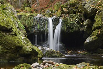 Waterfall falling into a moss-covered grotto, surrounded by autumn leaves, Bavarian Forest National