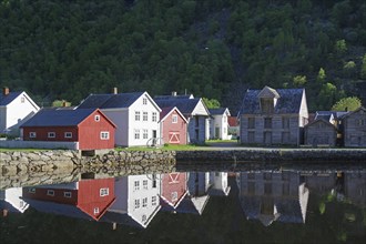 A small village with red and white houses reflected in the calm fjord waters, heritage-protected