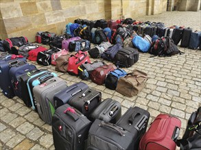 The luggage of a group of travellers stands in rows on the pavement, outside, suitcases and bags