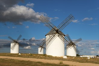 White windmills under a clear blue sky with scattered clouds. The surroundings are brightly lit and