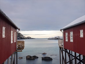 View between two traditional red wooden houses across the fjord to the mountains of the mainland,