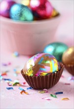 Small chocolate Easter eggs wrapped in shiny foil, placed on a bed of shredded pastel-colored