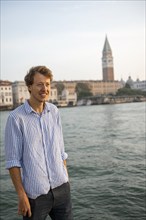 Young man in striped shirt and shorts on the banks of the Grand Canal, behind Campanile, Venice,