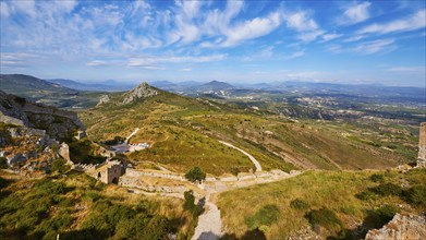 Wide view of a hilly landscape with path and ruins under a blue sky with clouds, Archaic Castle,