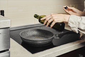 Unrecognizable woman pouring olive oil on frying pan from the bottle