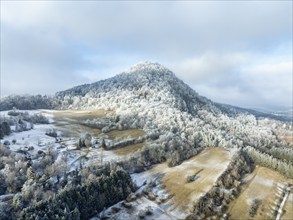 Aerial view of the snow-covered Hegau volcano Hohenhewen, surrounded by frosty trees in a winter