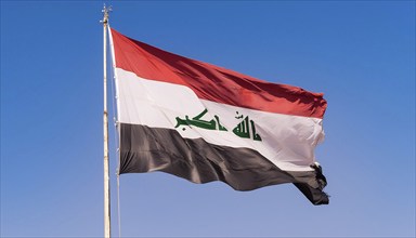 The flag of Iraq flutters in the wind, isolated against a blue sky