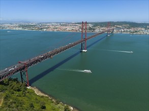 Red bridge spanning the water, lined with boats, with a city and nature in the background on a