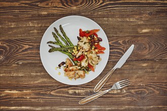 Overhead view of spicy chicken stew with vegetables and fried asparagus on wooden table