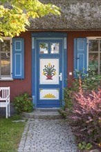 Colourful front door of a thatched roof house with decorative carving and painting, flower motif,