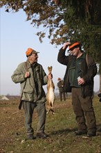 Hunter with hunted hare (Lepus europaeus) receives a hunter's greeting from a hunting companion,