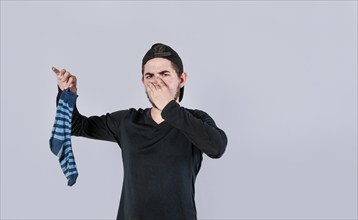 Man holding sock covering his nose isolated.Teeneger holding a stinky sock isolated. smelly socks