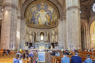 Church interior with a large mosaic of Jesus above the altar, people praying, Paris