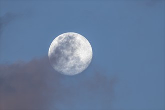 Full moon behind a cloud and blue sky