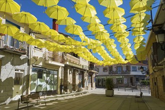 Sunny alley with yellow hanging umbrellas as decoration, surrounded by various houses under a clear