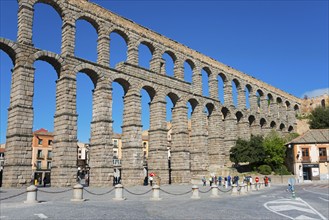 Majestic ancient aqueduct framed by buildings and tourists under a blue sky, Aqueduct, Segovia,