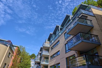 Modern residential building with several balconies and glass railings under a blue sky with clouds