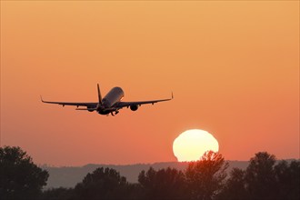 An aeroplane flies in the sunrise sky, surrounded by intense orange tones, passenger plane after