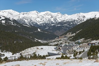 Blick auf eine verschneite Berglandschaft mit Wäldern und Straßen unter einem klaren blauen Himmel,