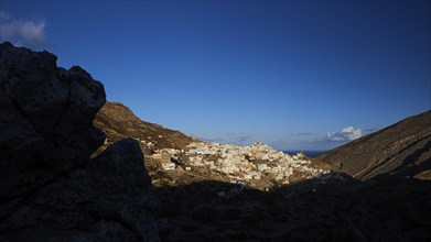 A village in the early morning light, surrounded by dark hills and rocks, illuminated by moon or