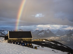 Mountain hut on top of mountain Fannaråken, storage hut, rainbow over Jotunheimen peaks,