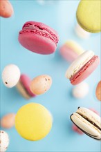 Multicolored flying macaroons and chocolate eggs frozen in the air on blurred blue background. top