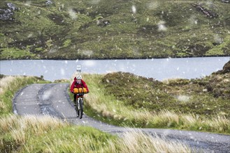 Lonely biker cycling through the Scottish Highlands on heavily laden touring bicycle along single